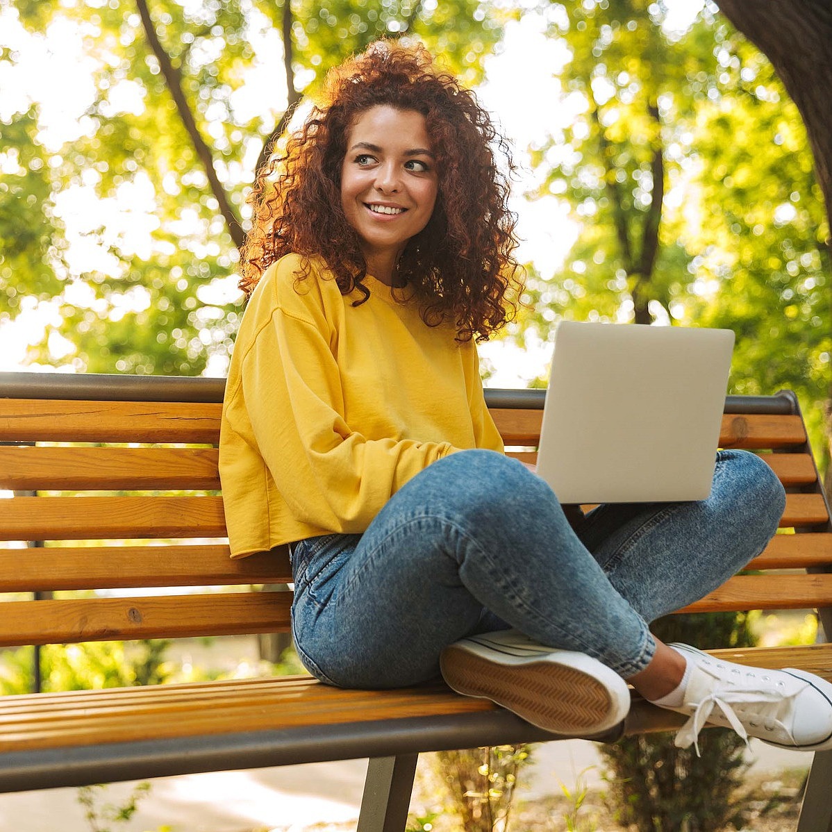 Junge Frau sitzt mit einem Laptop auf einer Parkbank
