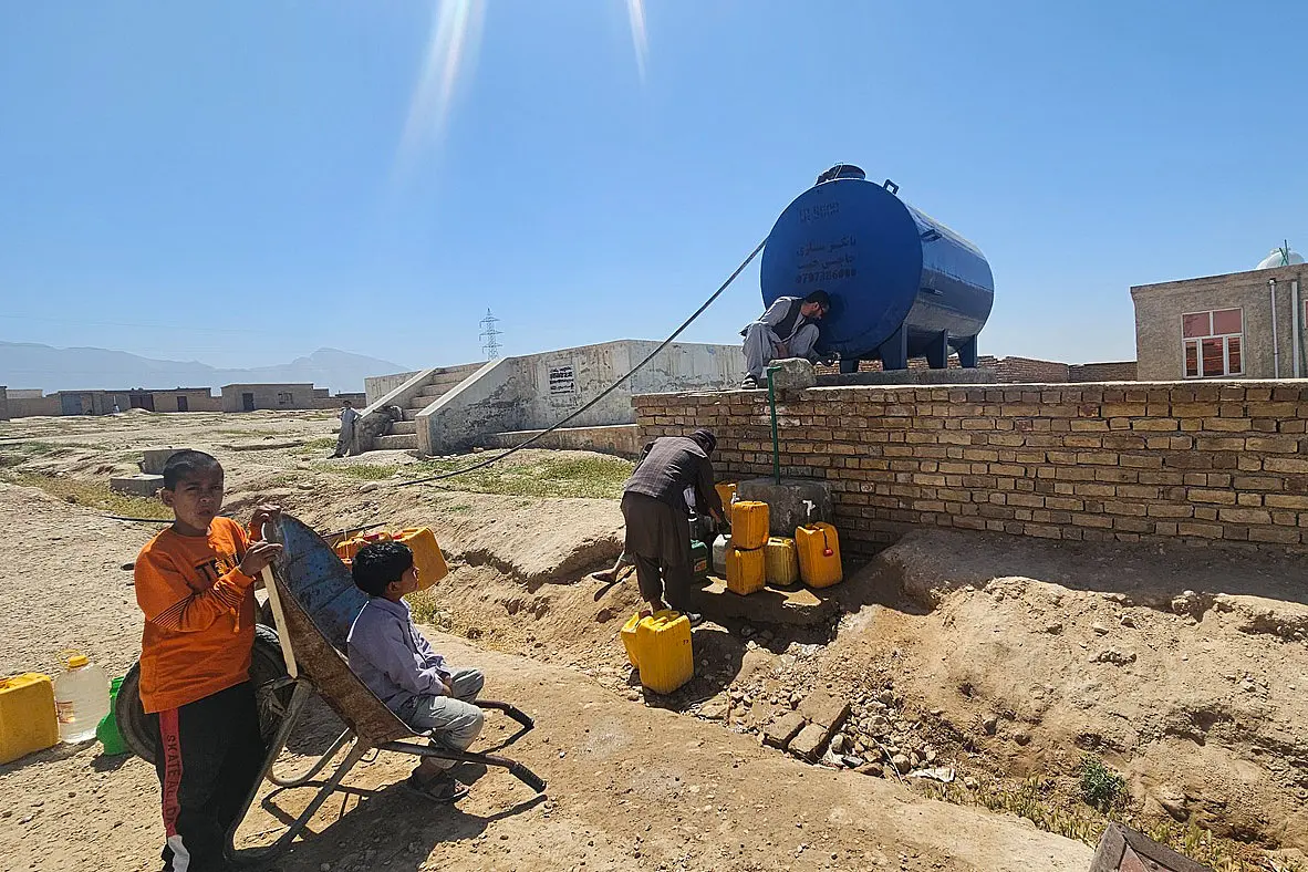 Neuer großer Wassertank und zwei Menschen, die Trinkwasser holen